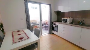 A compact kitchen with a microwave, sink, and oven. There is a dining area with a table and chairs. - CRISTIANO´S apartment with terrace in Alcochete (Alcochete)