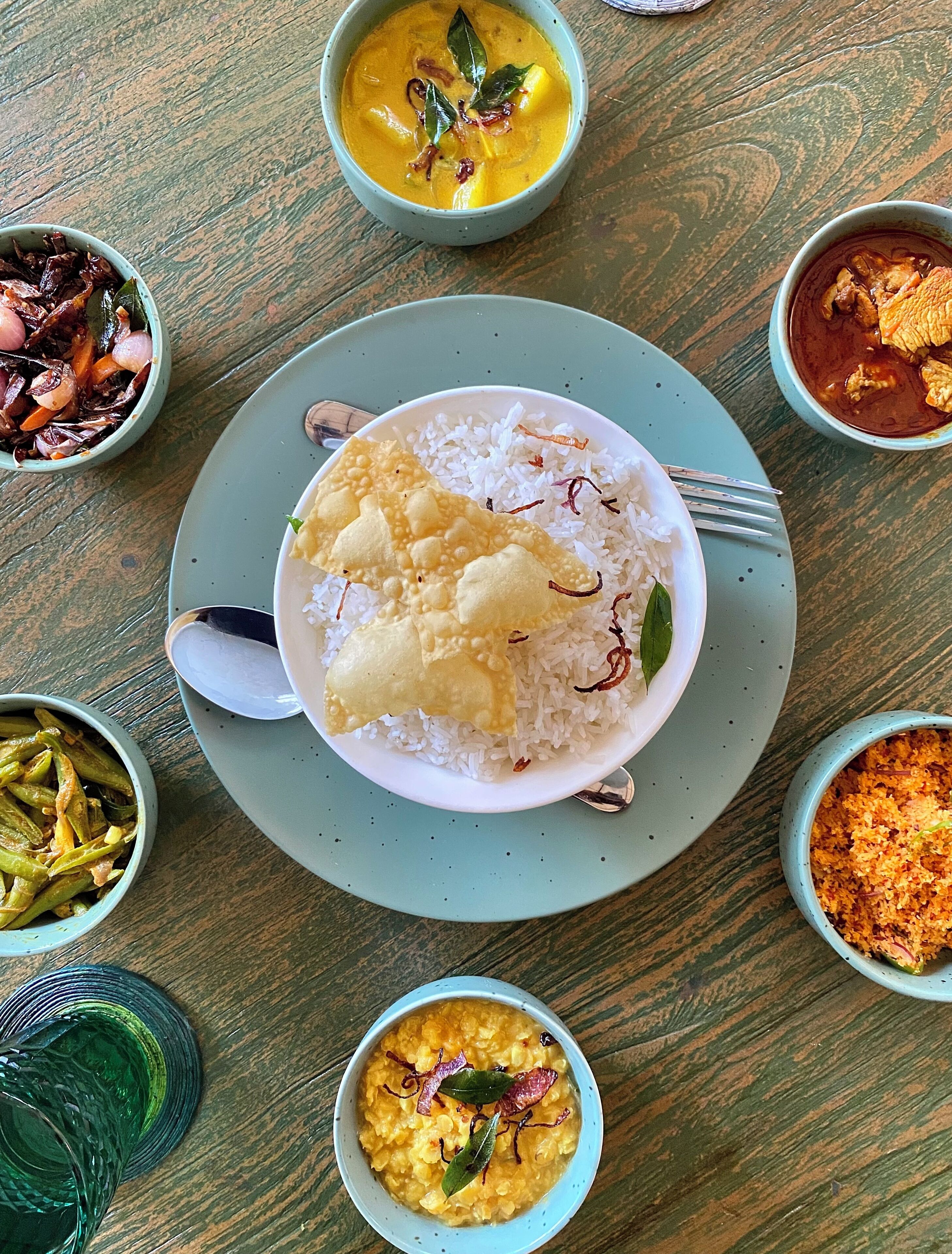 A table with a plate of white rice and a piece of fried food, surrounded by various bowls of different dishes.