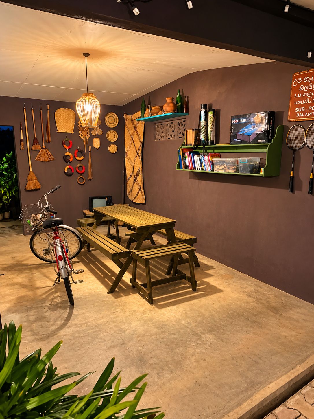 A room with a wooden table and benches, a bicycle, and shelves with books and decorative items.