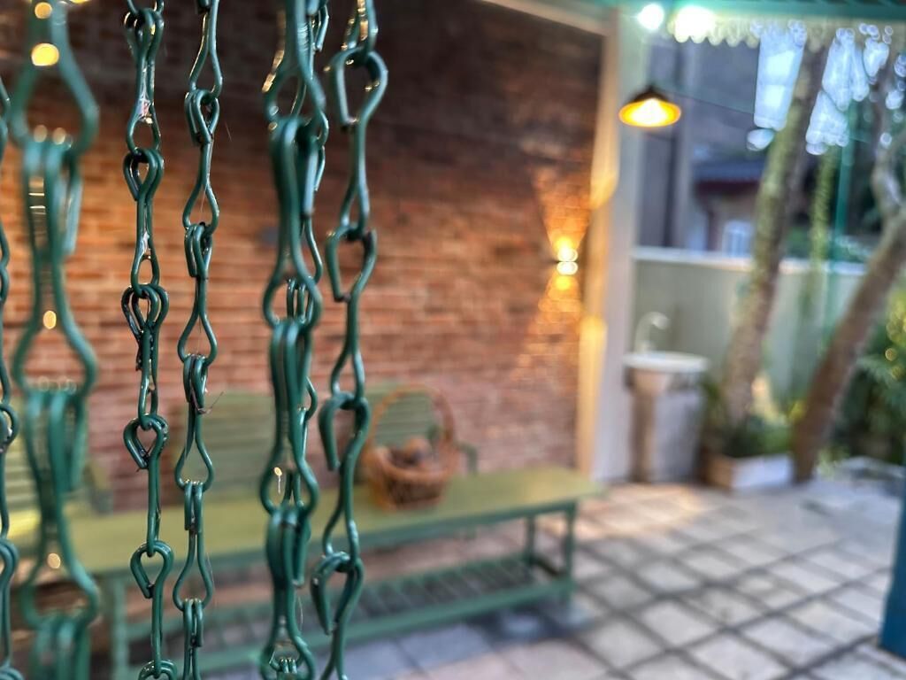 A close-up of a green metal fence with a brick wall and a bench in the background.