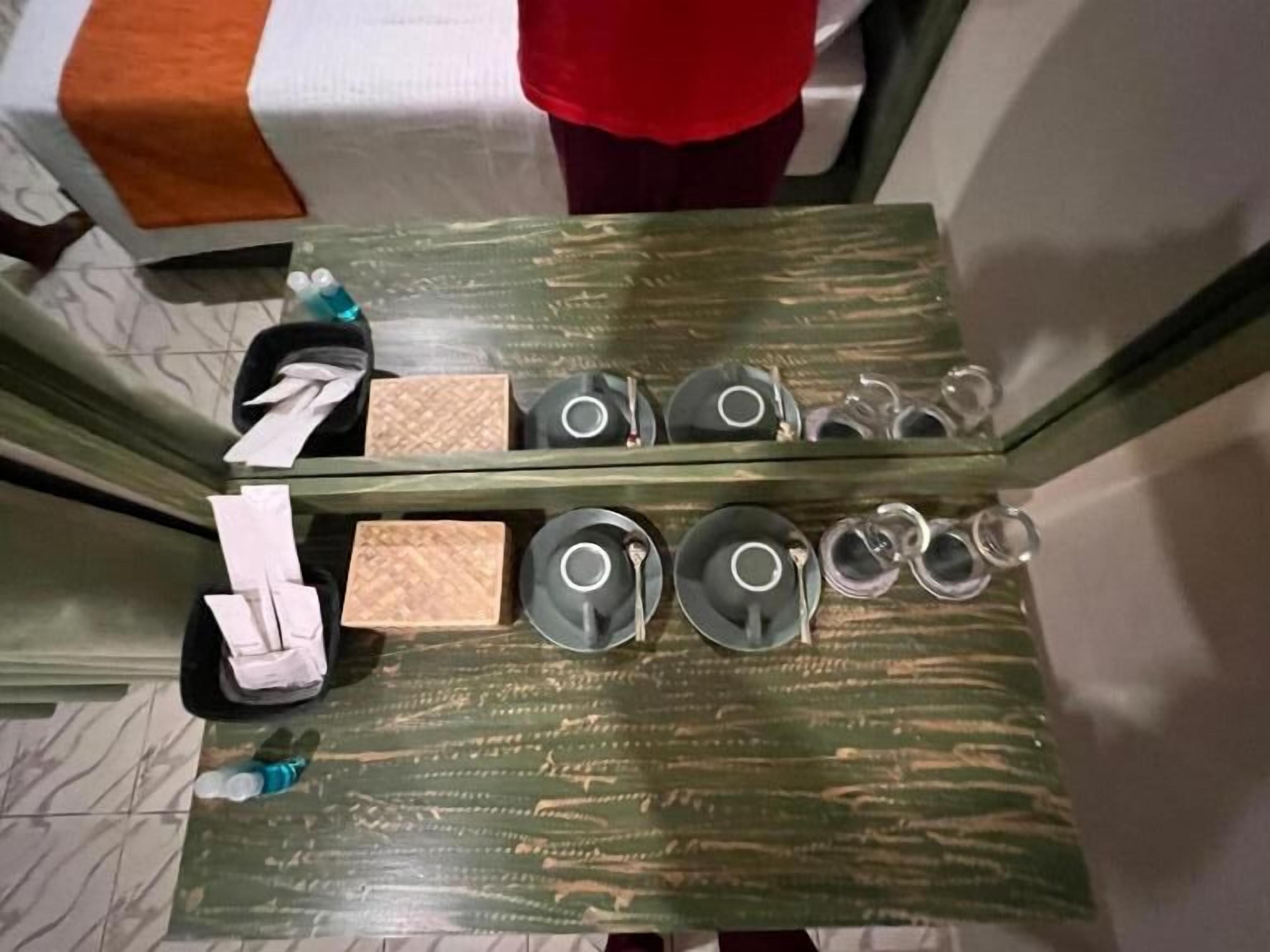 A table with a green textured surface, a tissue box, a water bottle, and several teapots and cups arranged on it.