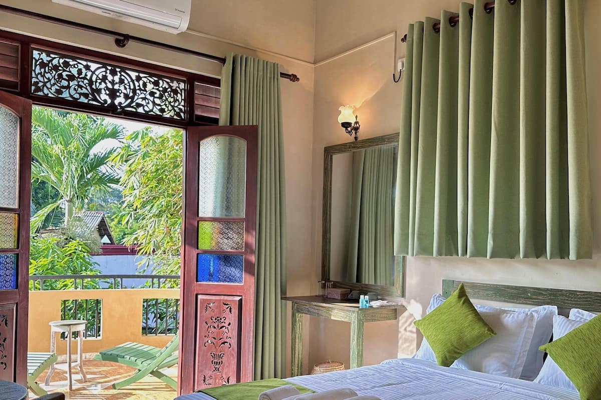 Une chambre d’hôtel avec un lit, un bureau, une chaise et une vue sur la verdure.