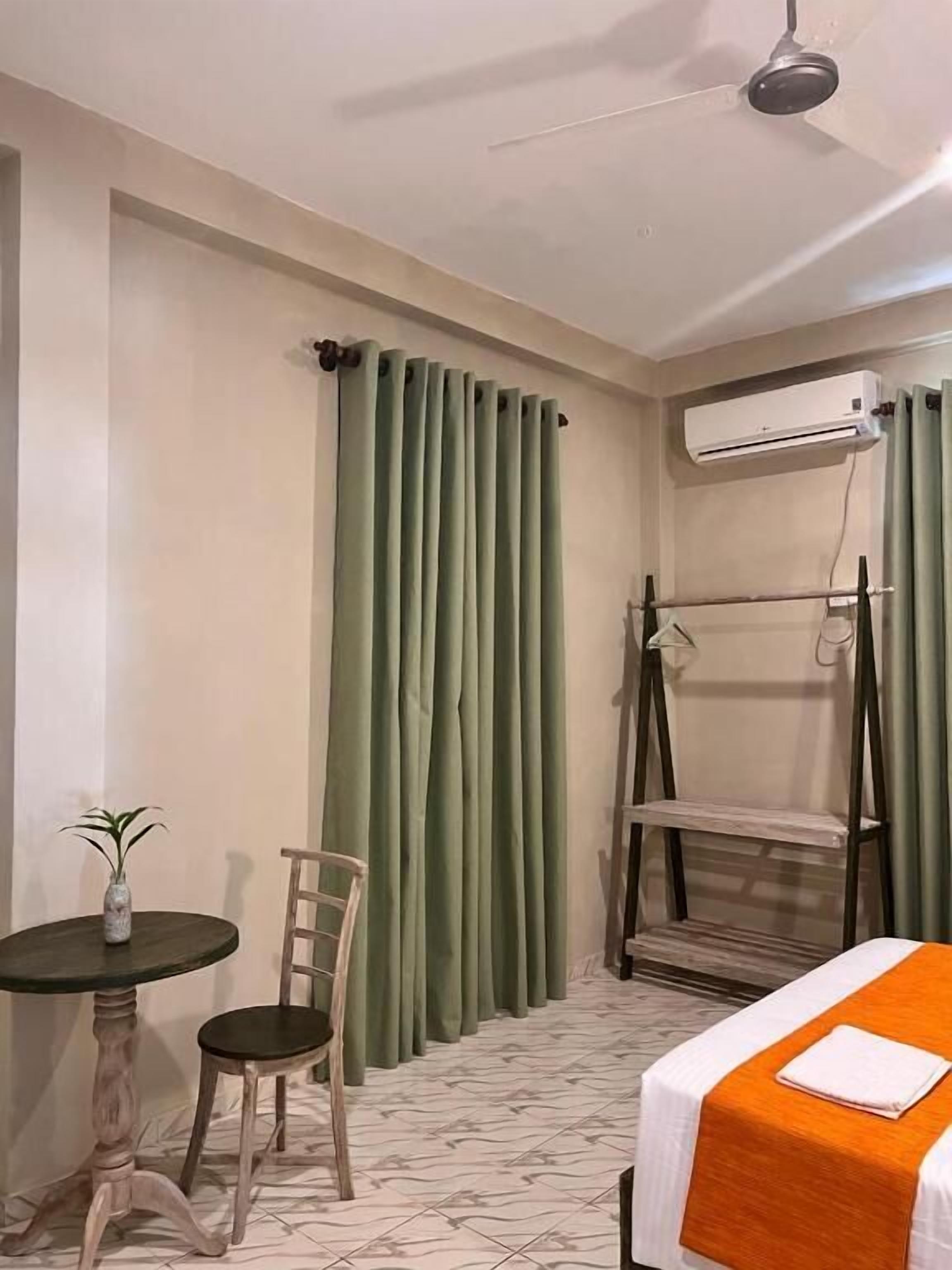 A hotel room with a bed, a small table with a chair, a hanging chair, and a potted plant.