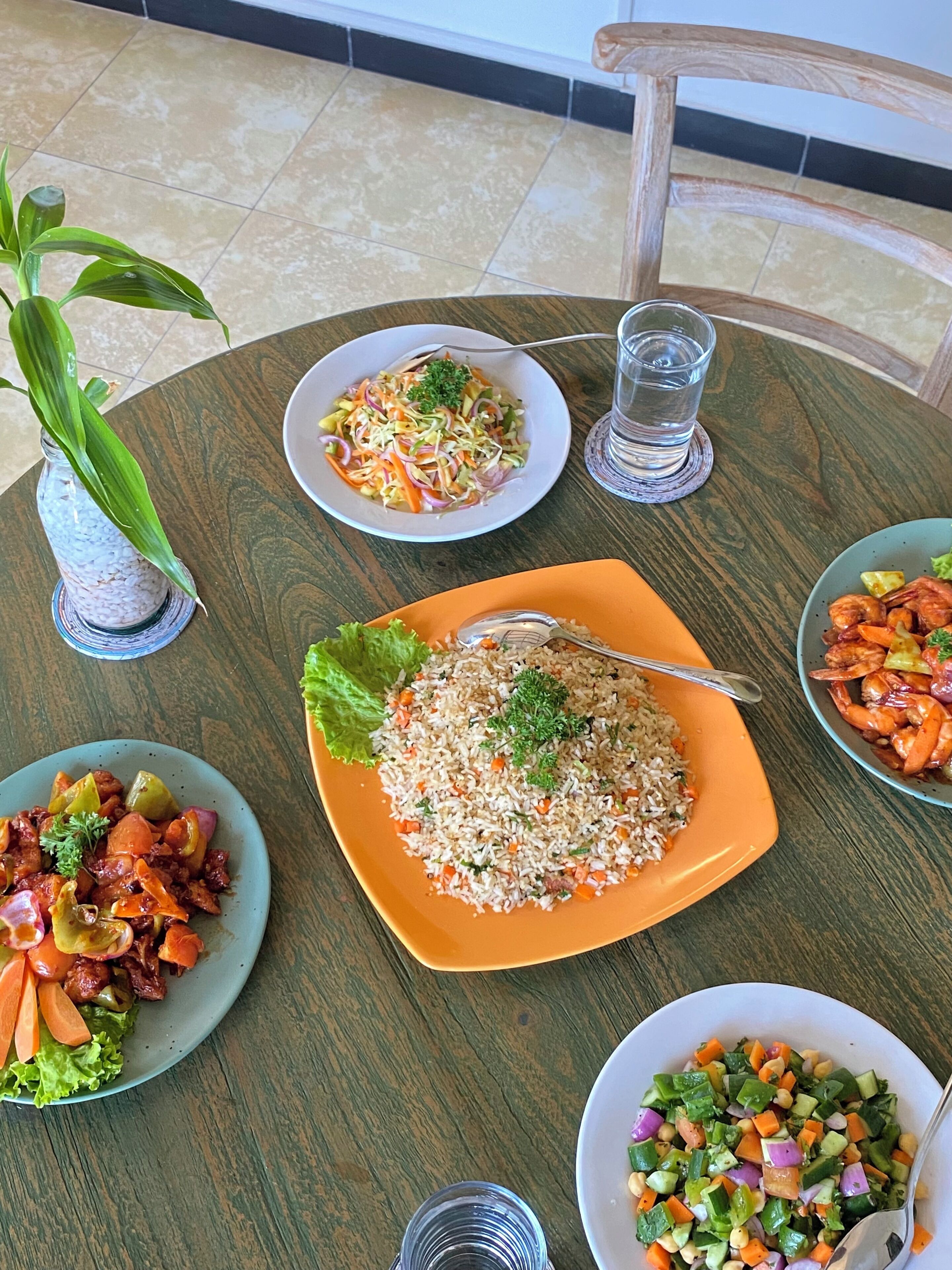 A dining table with various dishes, including a plate of fried rice, a salad, and a shrimp dish.