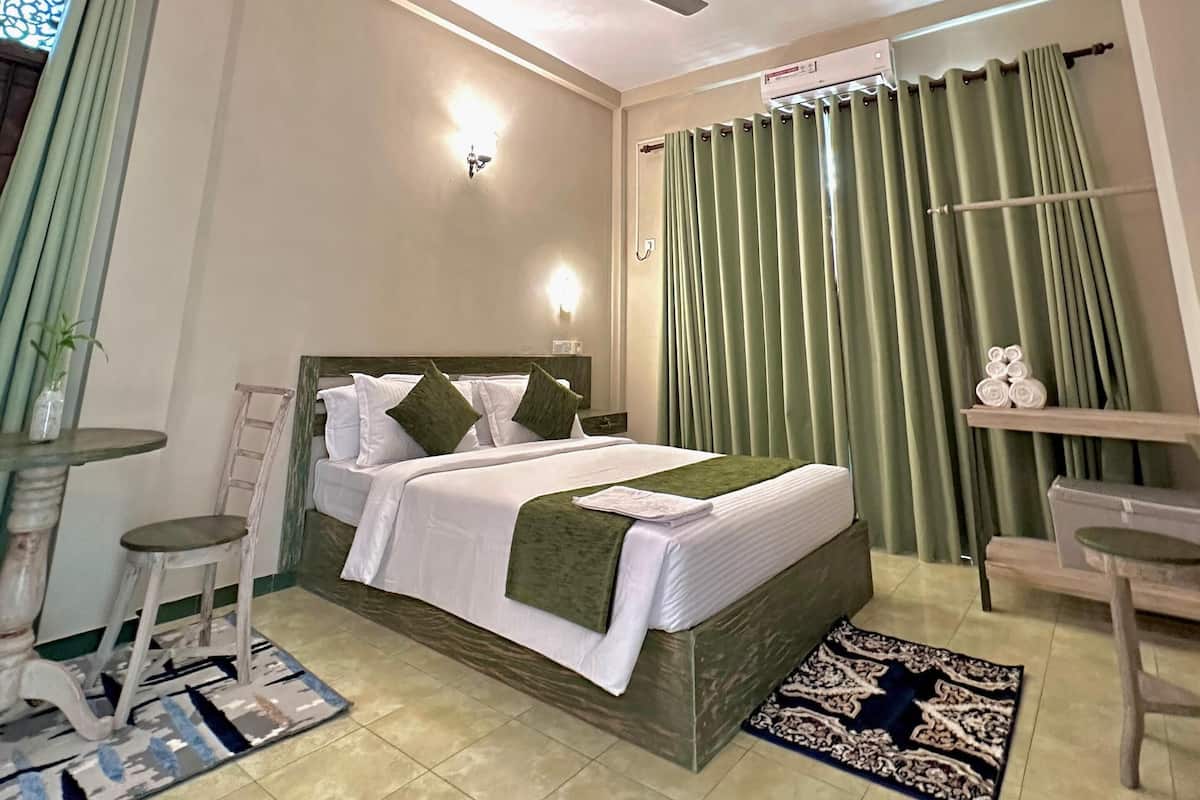 Une chambre d’hôtel avec un lit, un ventilateur de plafond, une table de chevet, une table et une chaise.
