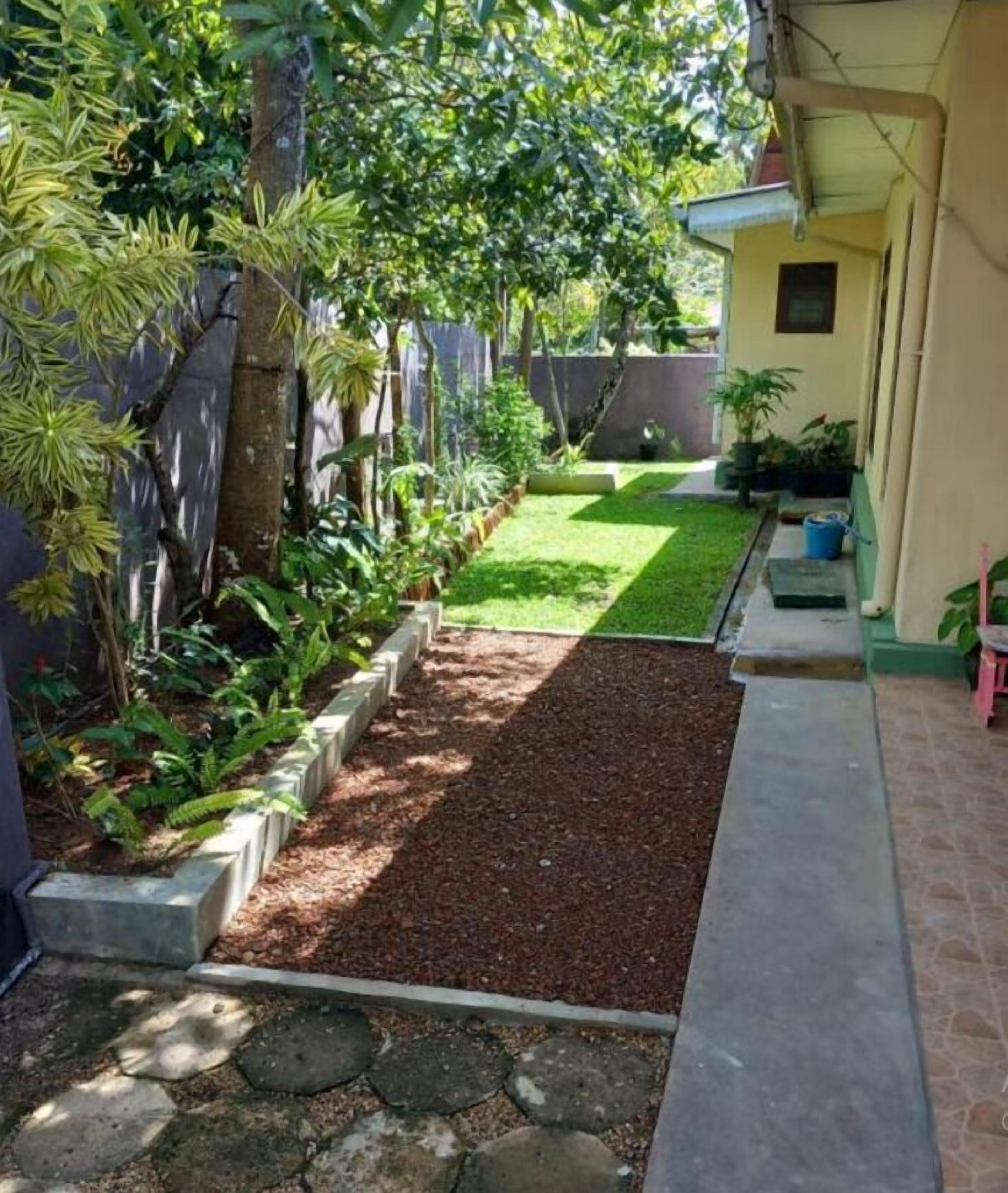 A narrow pathway leading to a small grassy area with a concrete border and a stone pathway.