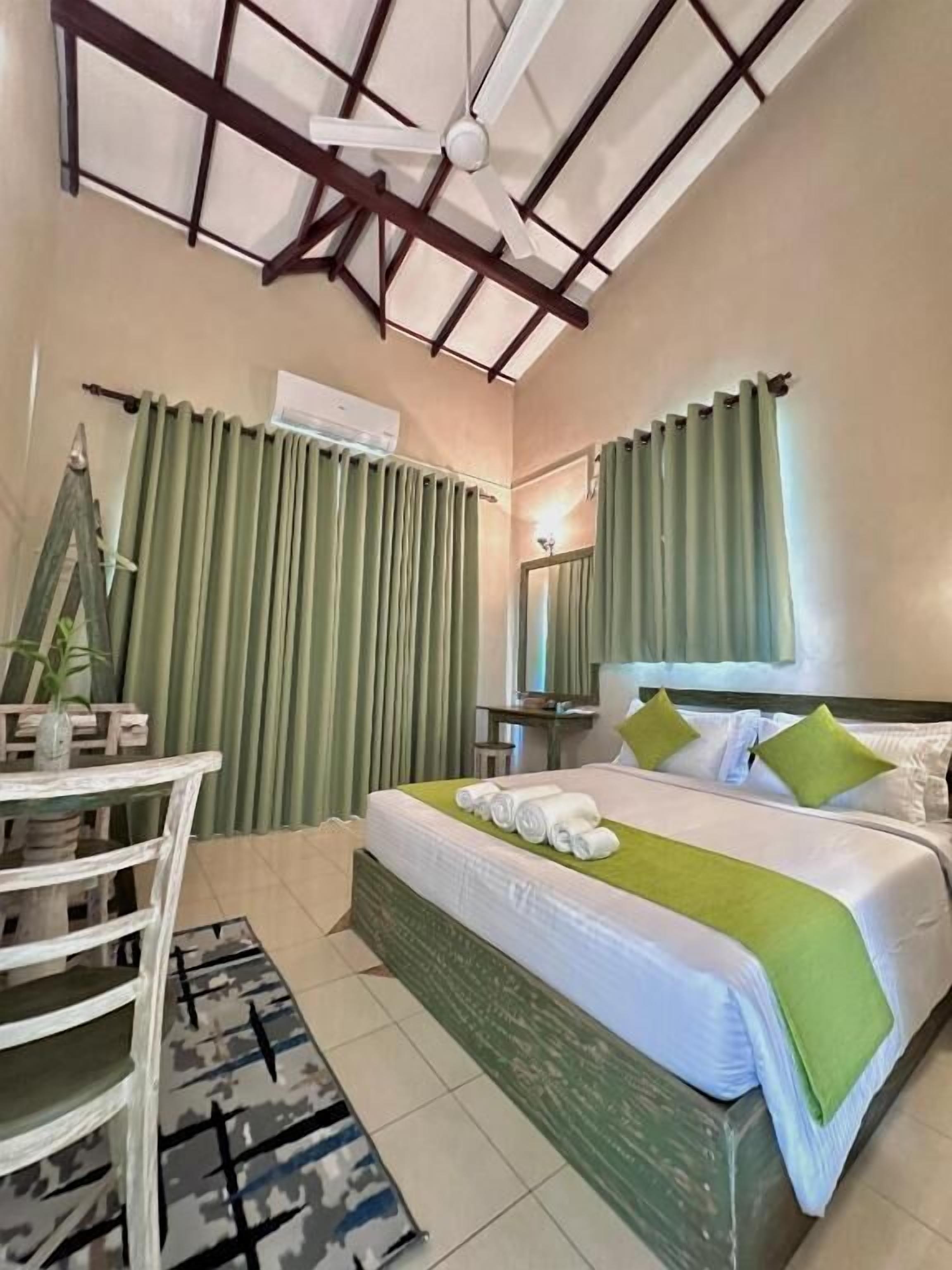 A hotel room with a bed, a desk, a chair, a mirror, and a ceiling fan.