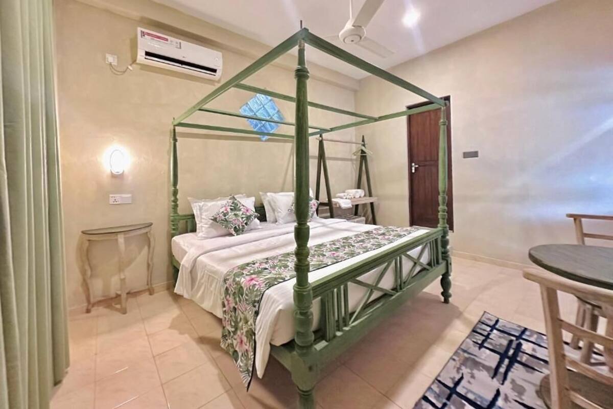 Un lit à baldaquin avec un cadre vert, une table de chevet, une chaise et une petite table surmontée d’un tapis à motifs.