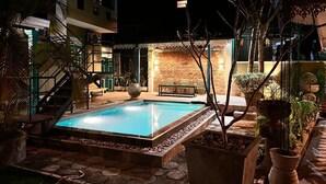 En swimmingpool med en stenkant, omgivet af plantede krukker og en murstensmur.