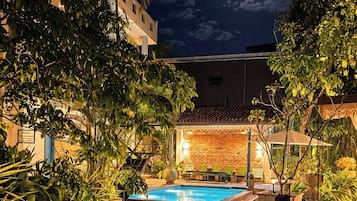 Un área de piscina exterior iluminada por la noche, con un muro de ladrillo y cielo despejado.