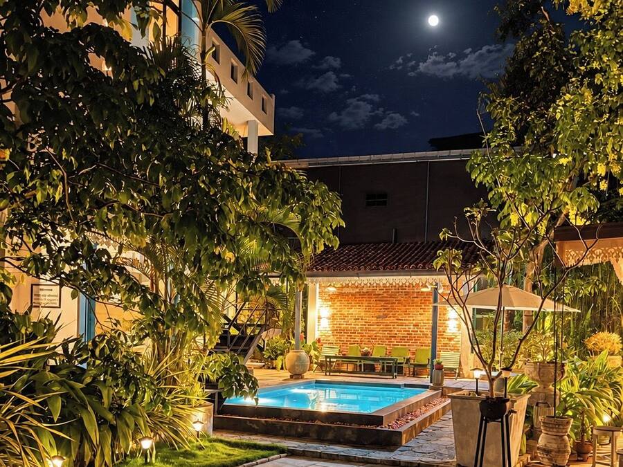 Un área de piscina exterior iluminada por la noche, con un muro de ladrillo y cielo despejado.