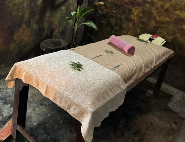 Una mesa de masaje con una toalla color beige, una toalla enrollada y una pequeña planta.
