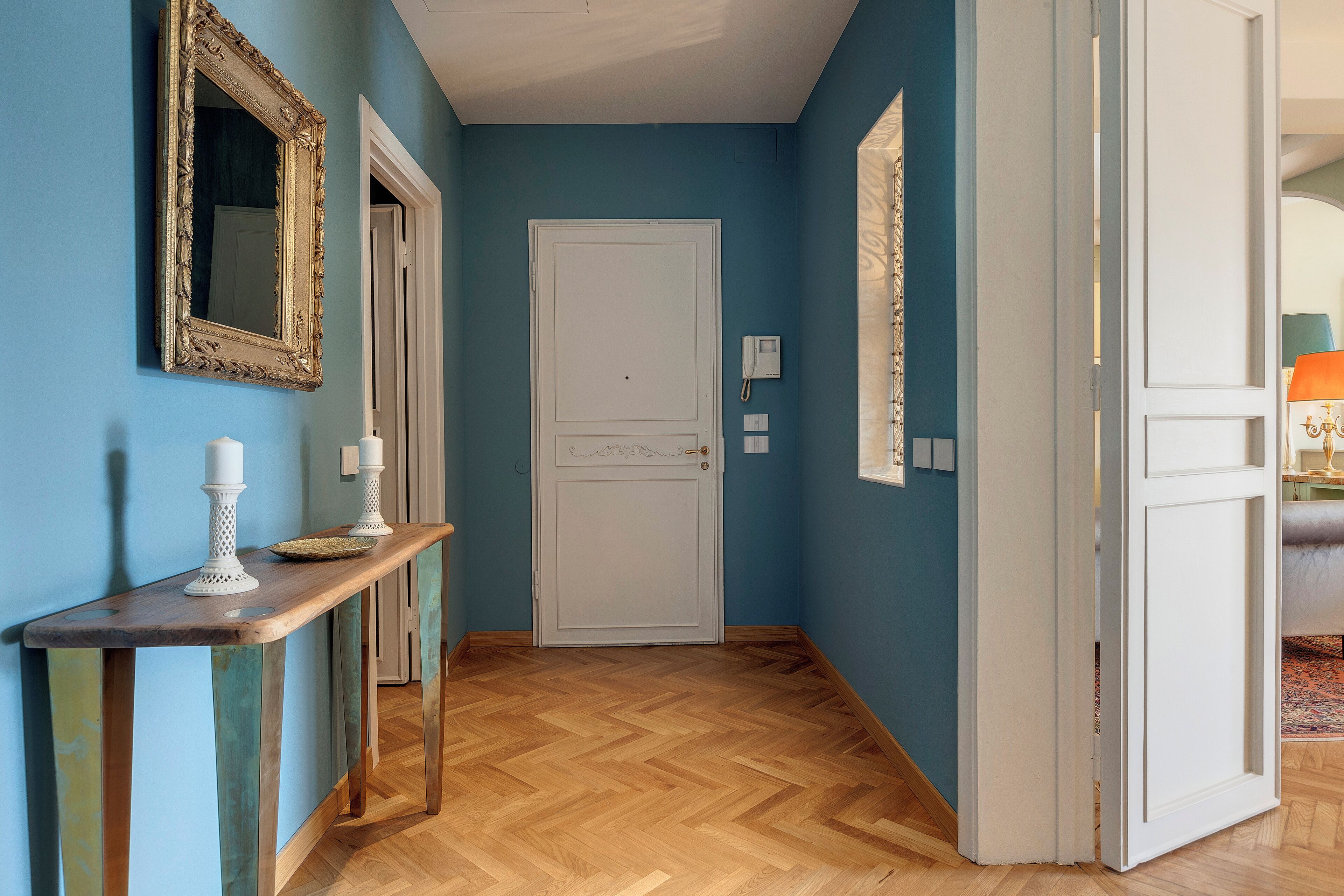 A hallway with a wooden console table, a white door, and a mirror on the wall.