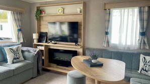 Ett modernt vardagsrum med en platt-TV, trähyllor, en soffa och ett runt bord.