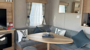 En modern inredning i en husbil med en grå soffa, ett träbord och en tv som står på ett stativ.