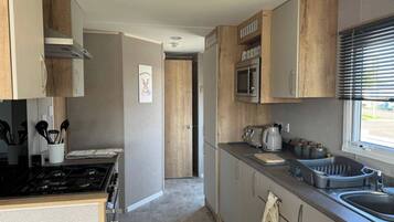 A modern kitchen with a stove, microwave, and sink. There is a window with blinds, and a door leading to another room.