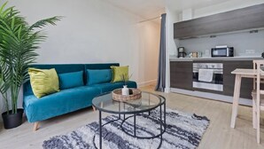 A modern living room with a teal sofa, a glass coffee table, and a large potted plant. - Apartment Birmingham City (Birmingham)