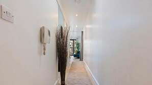 A narrow hallway with white walls, a light switch, a telephone, and a decorative plant. - Apartment Birmingham City (Birmingham)