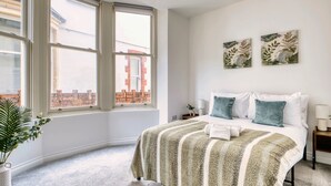 Ein Schlafzimmer mit einem großen Fenster, einem Bett mit gestreifter Decke, zwei Kissen und zwei an der Wand befestigten Kunstwerken.