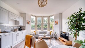 Eine moderne Küche mit weißen Schränken, ein Essbereich mit einem Marmortisch und ein Wohnzimmer mit einer Couch und Fernseher.