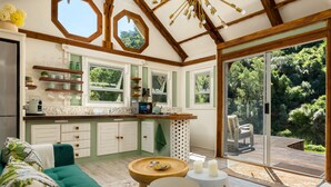 A modern kitchen with wooden beams, green cabinets, and a large window overlooking a garden. - Amazing Riverside Retreat With Hot Tub & Ecopool (Mossel Bay)