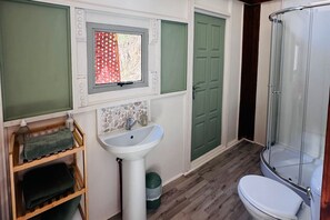 A bathroom with a white sink, green towels, a window with a red pattern, a green door, and a glass shower enclosure.