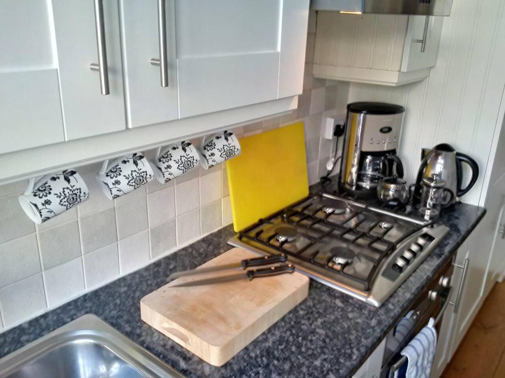 A kitchen with a gas stove, coffee maker, and a wooden cutting board.