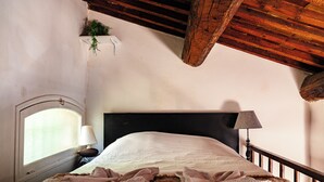 A bedroom with a large bed, a wooden ceiling, a small window, and a nightstand with a lamp. - Le Cardinale - A Journey to Provence (Aix en Provence)