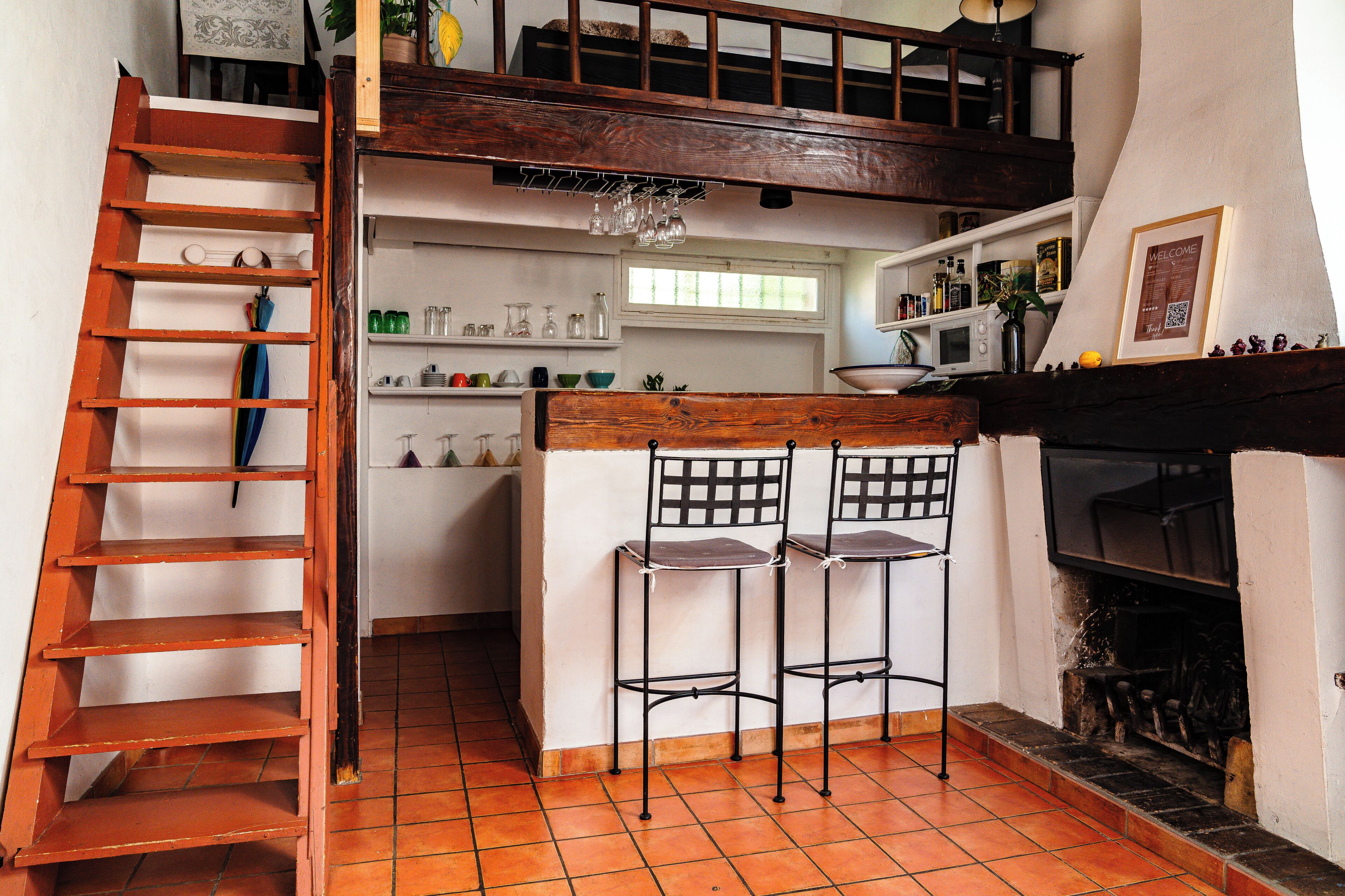 A kitchen with a wooden staircase, two bar stools, a microwave, and a fireplace.