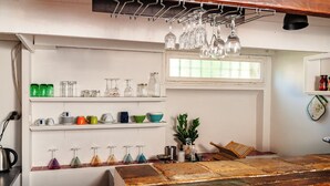 A kitchen with shelves holding various glassware and dishes, a window, and a wooden table. - Le Cardinale - A Journey to Provence (Aix en Provence)