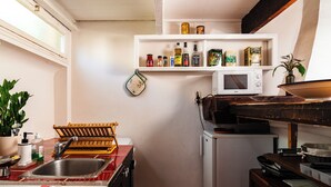 A compact kitchen with a white microwave, a sink, and a shelf above it holding various food items. - Le Cardinale - A Journey to Provence (Aix en Provence)