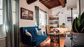 A cozy living room with a blue sofa, a dining table, and a bookshelf. - Le Cardinale - A Journey to Provence (Aix en Provence)