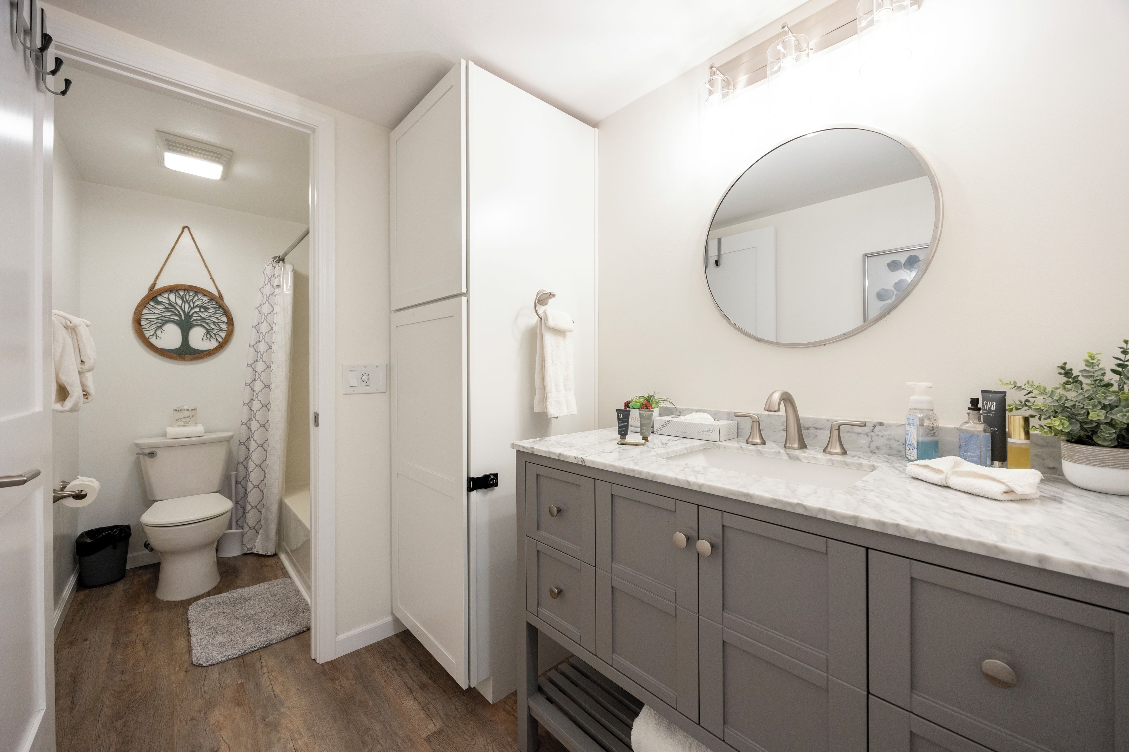 A modern bathroom with a marble sink, a round mirror, and a shower curtain with a tree design.