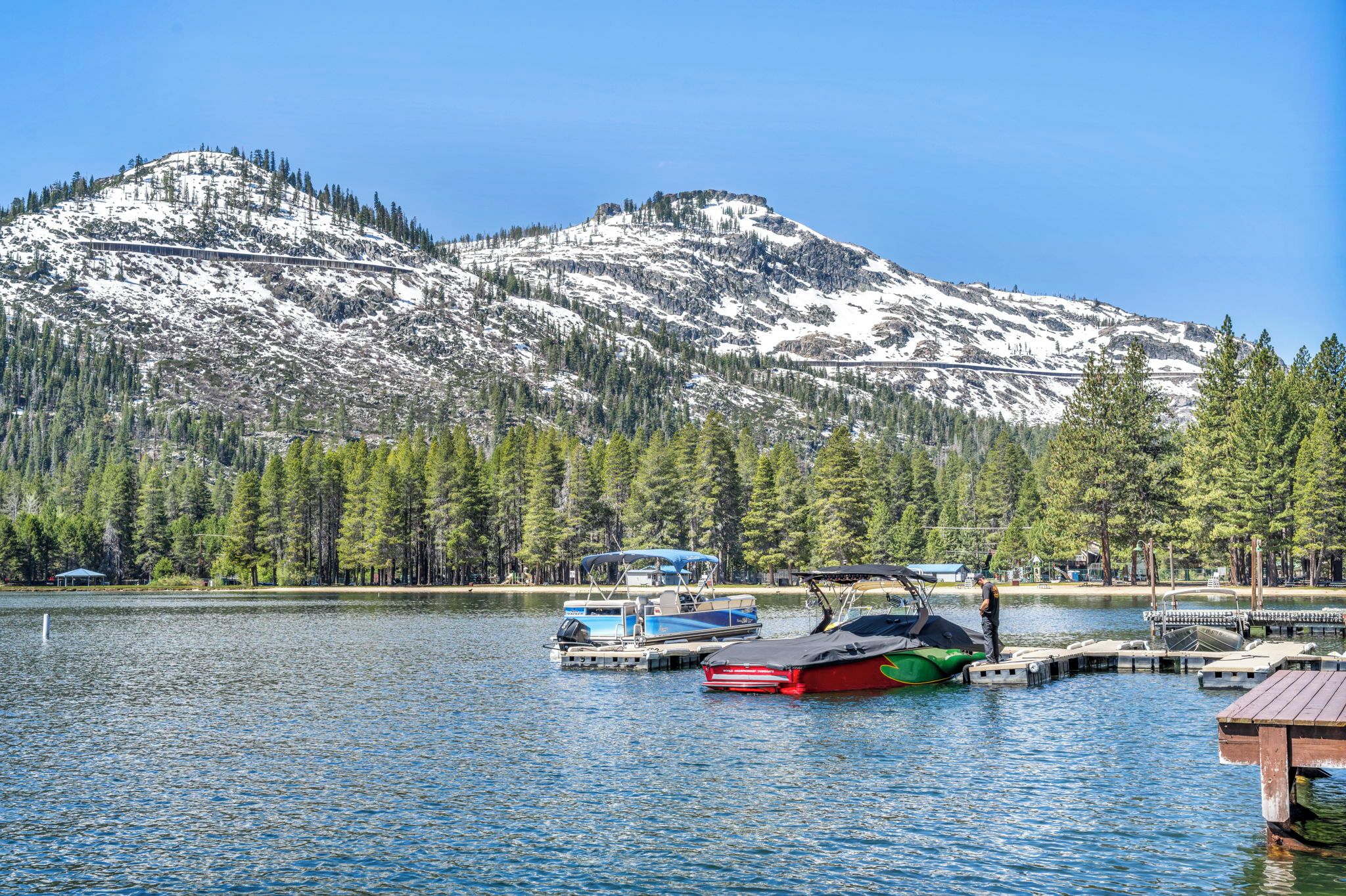 Um lago com barcos atracados, rodeado por montanhas cobertas de neve e floresta densa.