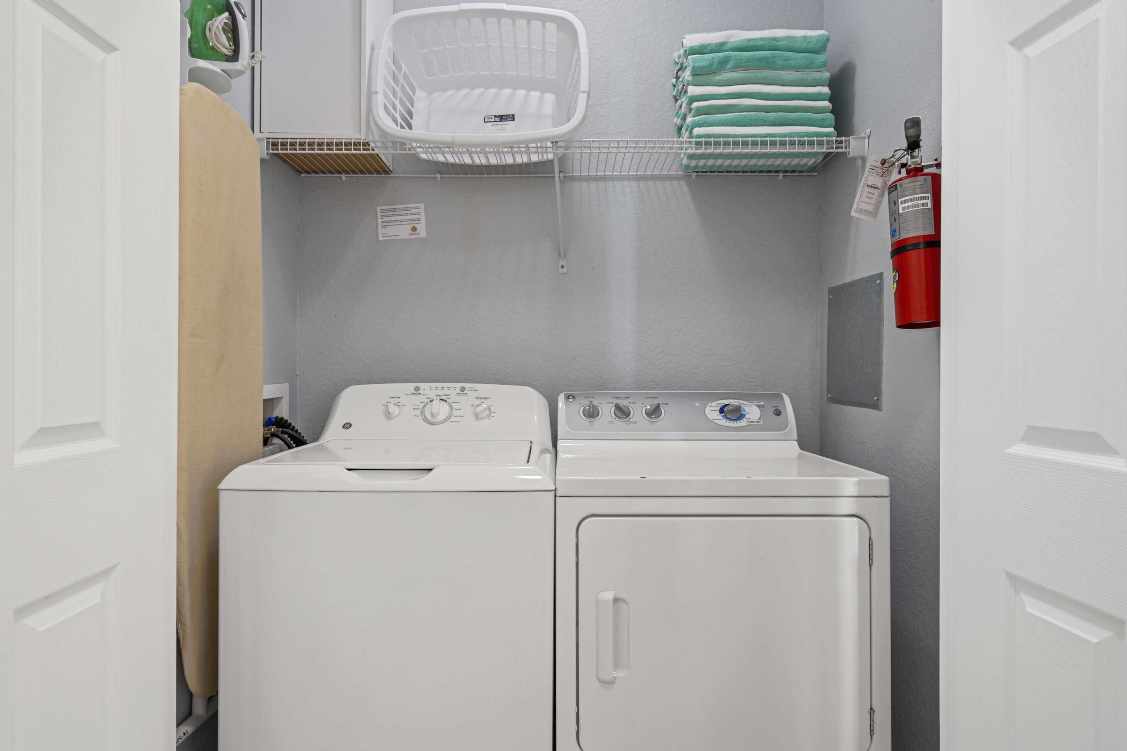Une buanderie équipée de deux machines à laver et deux sèche-linge superposés, d’un panier blanc posé sur une étagère et d’un extincteur fixé au mur.