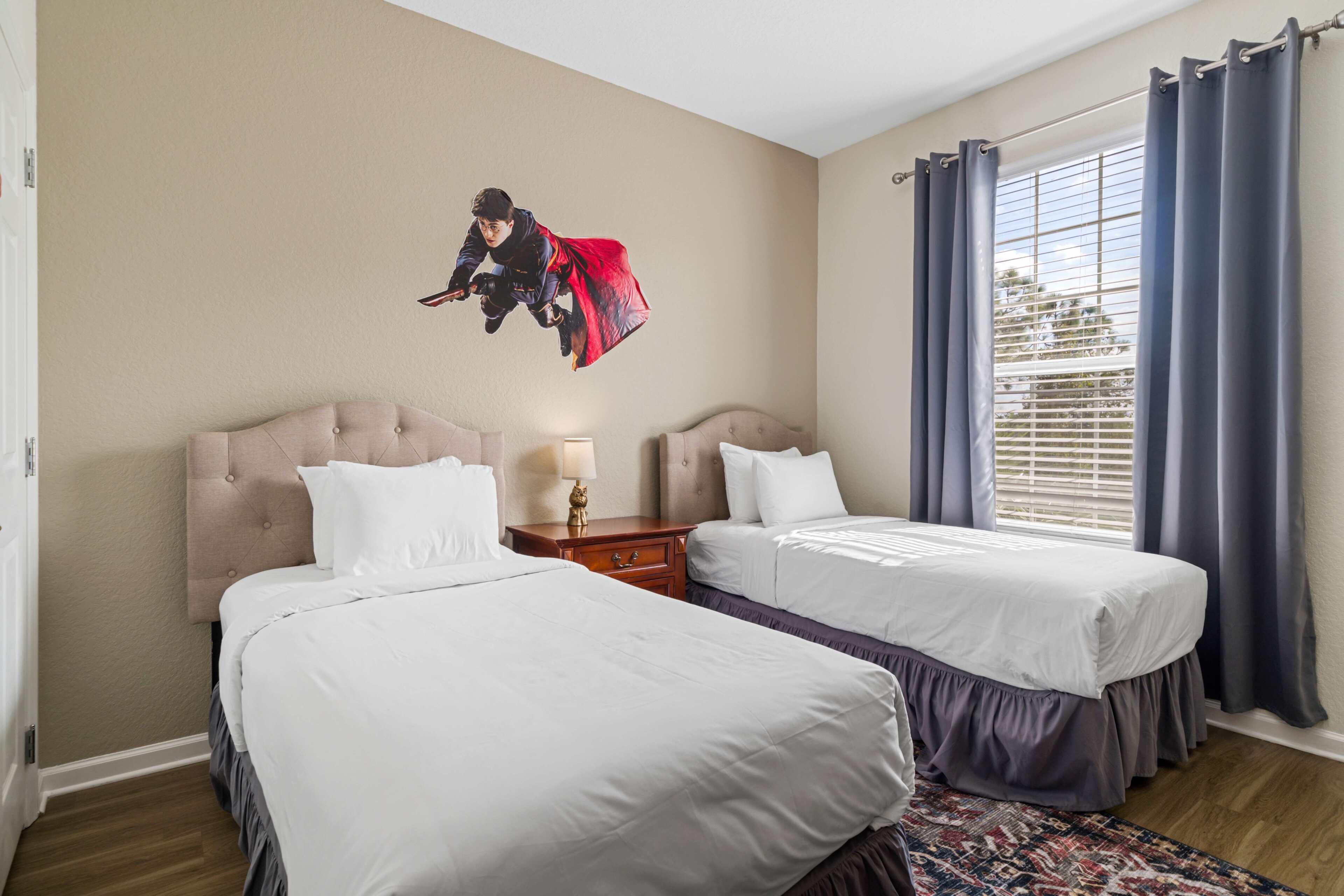 A hotel room with two beds, a headboard, a nightstand, a lamp, and a window with curtains.