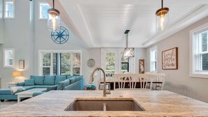 Una cocina moderna con encimera de mármol, lavamanos de acero inoxidable y luces colgantes.