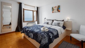 A bedroom with a bed, a window, a painting, a chair, and a radiator. - Pretty Apartment With Balcony (Porec)