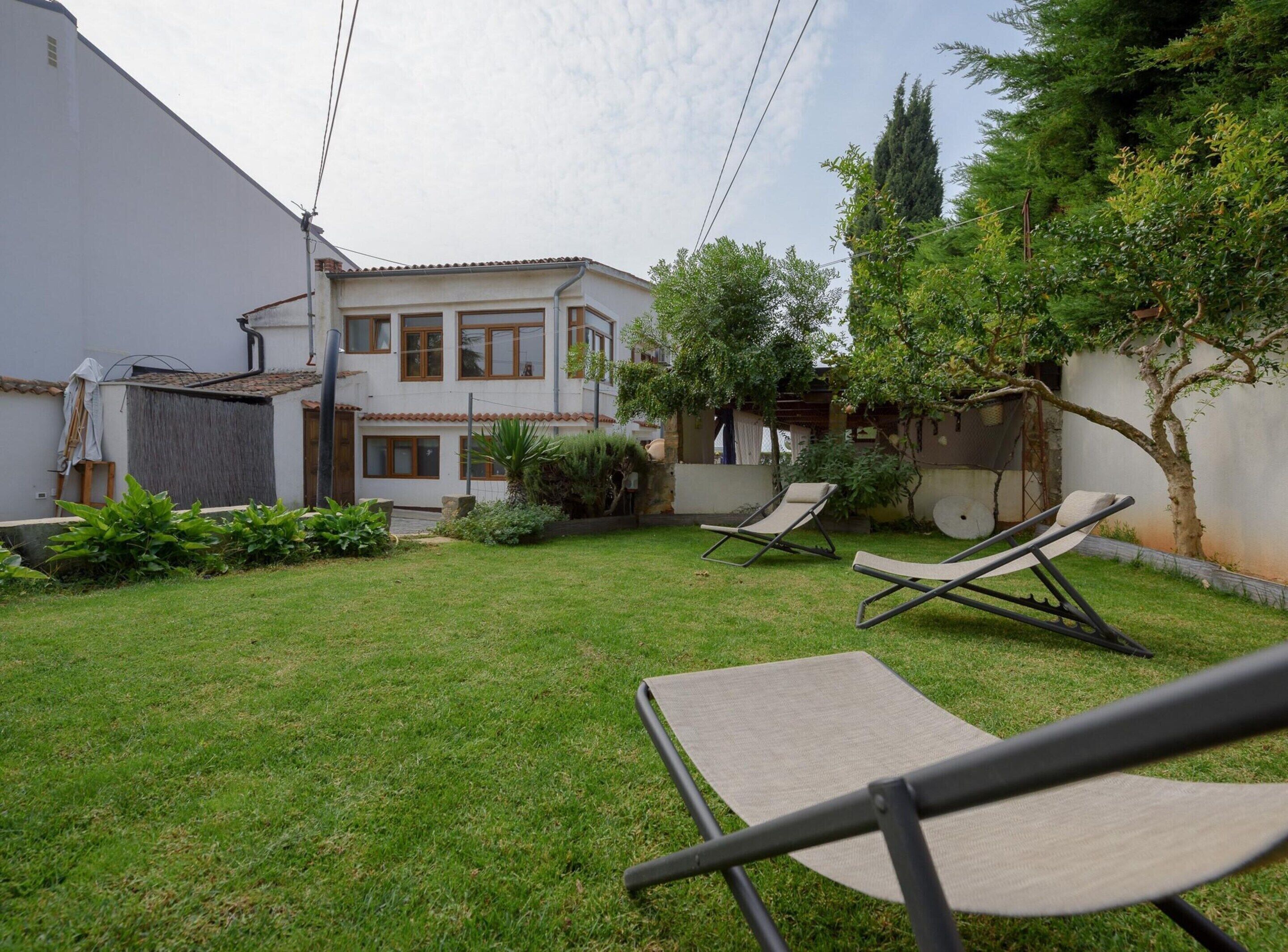 Una casa de dos pisos con un césped cuidado y dos sillones de descanso.