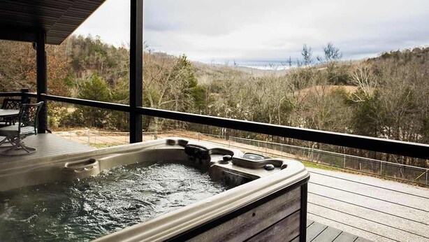 Ein Whirlpool auf einer Holzterrasse mit Blick auf eine bewaldete Landschaft.