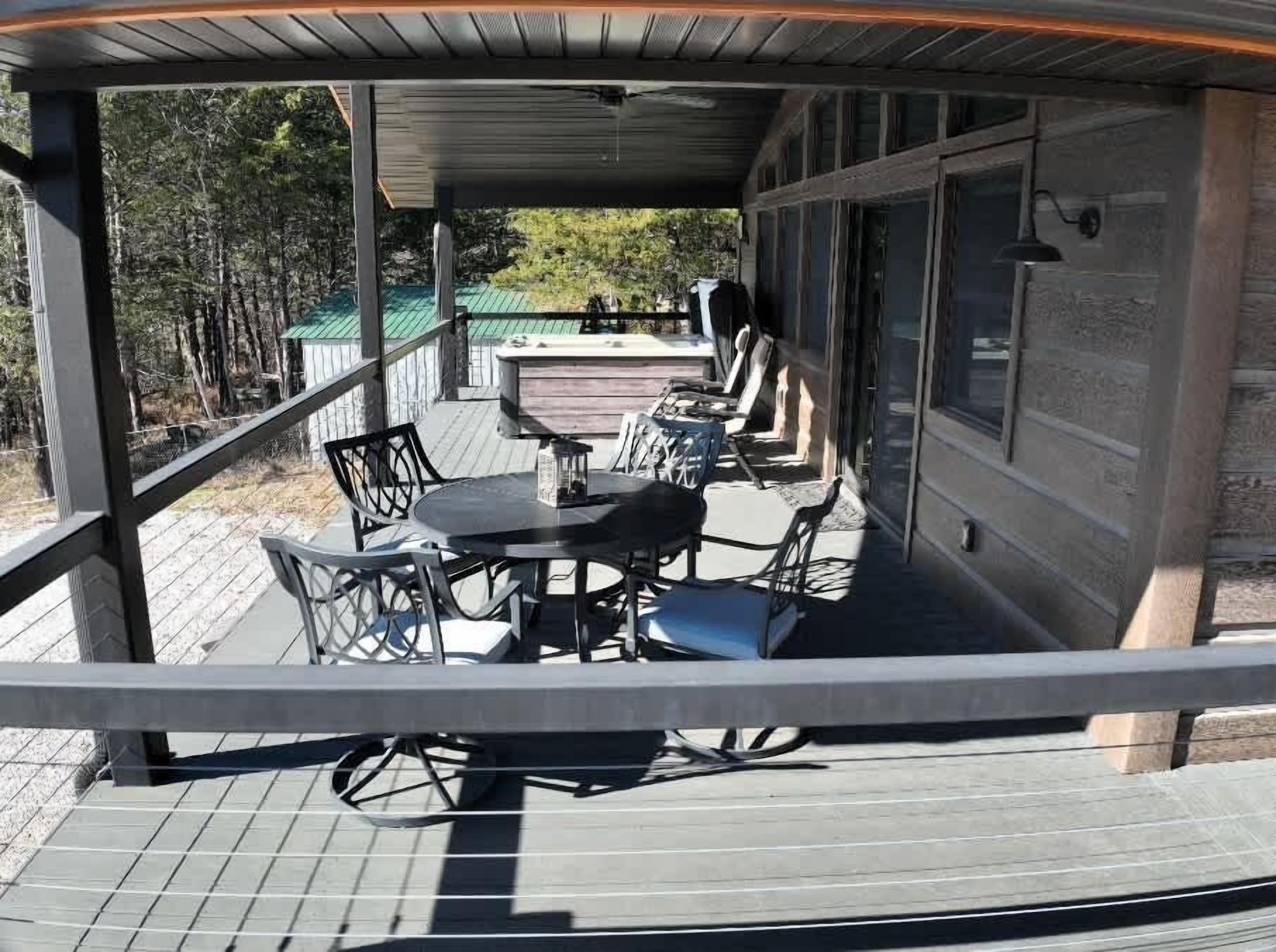 A covered outdoor seating area with a table and chairs, a hot tub, and a view of the surrounding trees.
