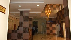 A hotel lobby with a checkered floor pattern, a chandelier, and a reception desk.