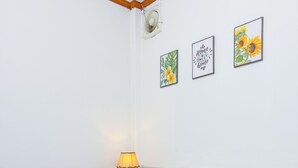 Un letto rifatto con lenzuola bianche, una lampada da comodino e tre quadri appesi al muro.