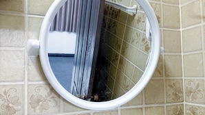 Un bagno con uno specchio rotondo, un water bianco e uno scaffale bianco.