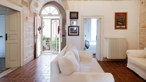A room with a white sofa, stone walls, a tiled floor, and a door leading to a balcony. - Dimora Signorile by Wonderful Italy (Polignano a Mare)