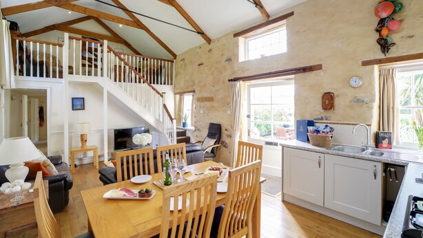 A spacious kitchen with wooden beams, a dining area with a table and chairs, and a staircase leading to an upper level.
