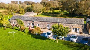 A stone building with a sloped roof, surrounded by a well-maintained lawn and parked cars.