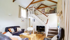 A spacious living room with a leather sofa, a wooden coffee table, and a black leather armchair. A staircase with white railings leads to an upper level.