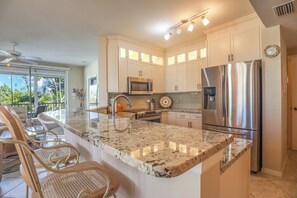 A modern kitchen with a large island, stainless steel appliances, and a dining area with wicker chairs.