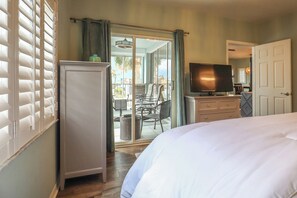 Habitación de hotel con cama, televisión, minibar y puerta corrediza de vidrio que da a un balcón.